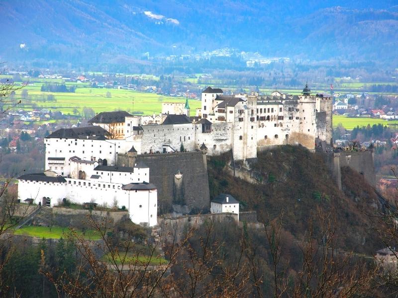 Elevation view of the white walls of Hohensalzburg Fortress sitting on the hill above Salzburg with the mountainside in the background