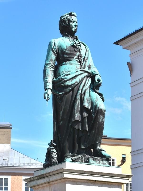 A green patinaed statue of Wolgang Amadeus Mozart sits in a square in Salzburg, Austria