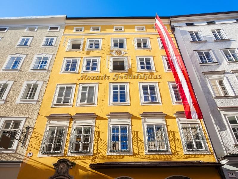 The yellow symmetrical front facade of Mozart's Birthplace museum in a row of buildings in Salzburg, Austria