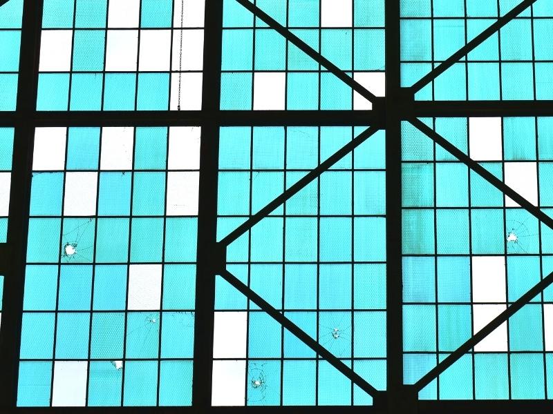 The light blue original glass panes, some with bullet holes, and modern clear glass replacement panes on the hangar doors at the Pearl Harbor Aviation Museum