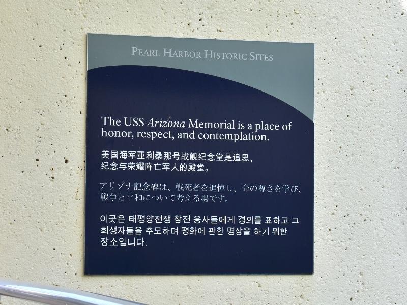 A simple blue and gray sign asks for respect in multiple languages before boarding the ferry out to the USS Arizona memorial