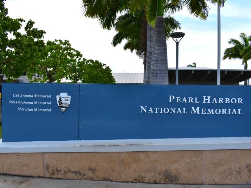 A dark blue entry sign for the Pearl Harbor National Memorial site, including the USS Arizona, USS Oklahoma, and USS Utah memorials