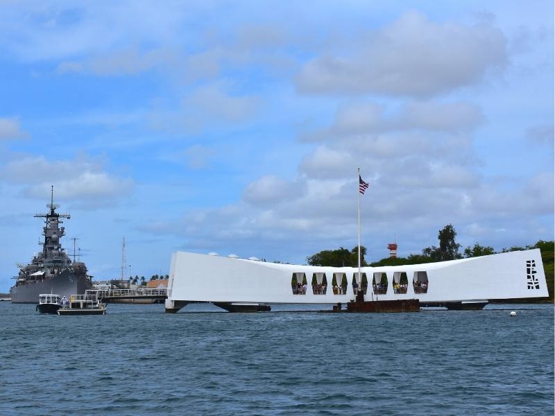 The bright white USS Arizona memorial sits atop the submerged ruins of the ship, still sticking out of the water, while the USS Missouri waits at anchor in the background