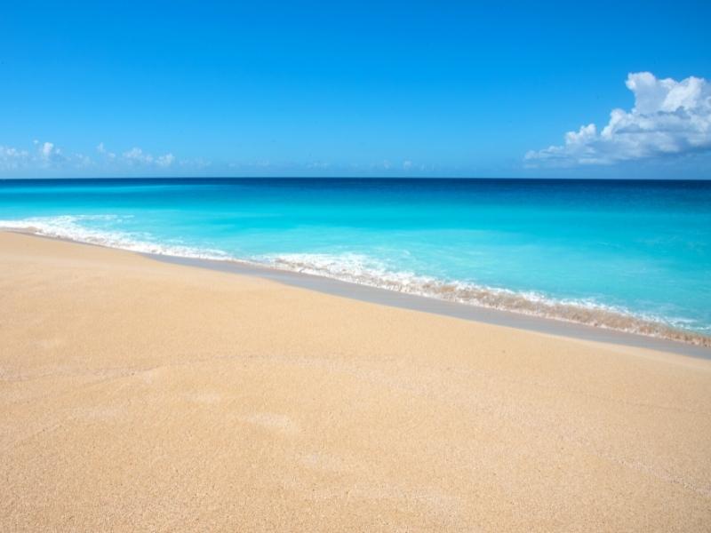 Smooth, sandy beach meets aqua blue waters of the Caribbean under a blue sky at Sandy Point Beach on St Croix