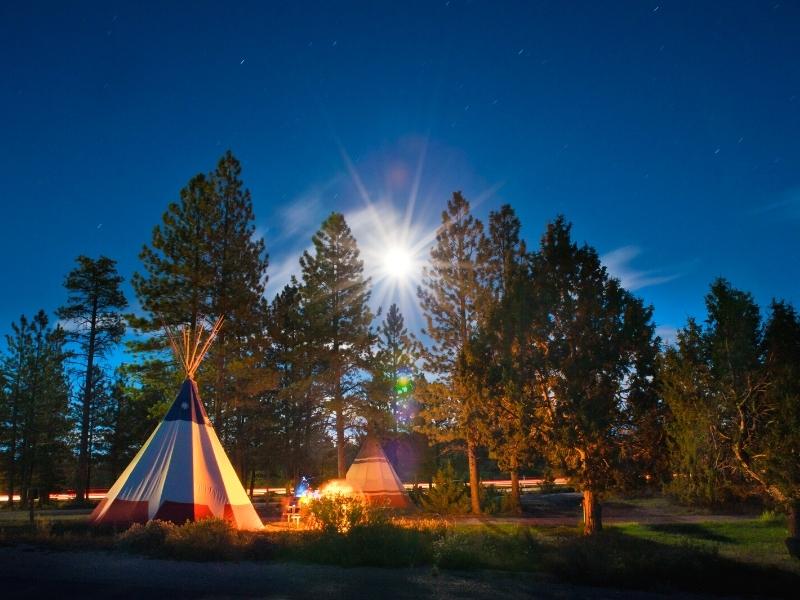 A teepee campsite glows amongst the pine trees as the moon rises at Ruby's Campground is a great place to stay in Bryce Canyon National Park