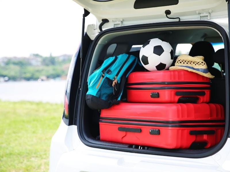 Red luggage, a blue backpack, a hat, and a soccer ball are packed into the trunk of a car
