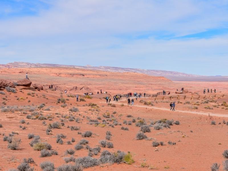 The Horseshoe Bend Overlook from afar, with people dotting the rim edge and climbing on boulders for different views.