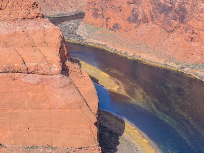 Zoomed in detail of the Horseshoe Bend promontory and the deep blue Colorado River water, tinged yellow along the shore