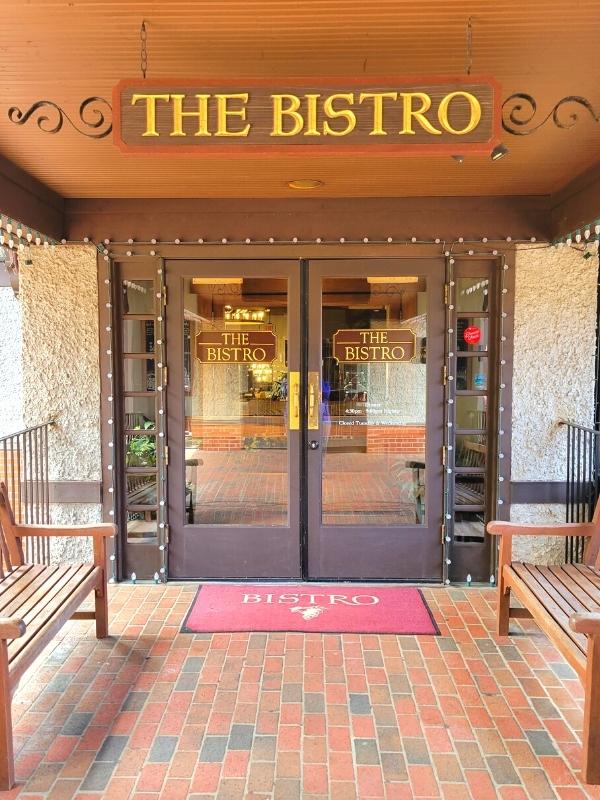 The Bistro at Biltmore, with doors lined with lights and two wooden benches flanking the door.