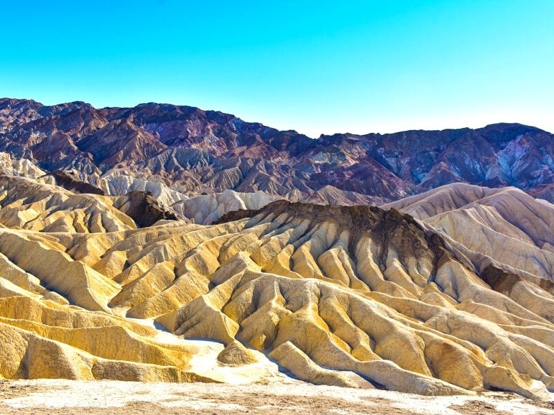 Zabriskie Point in Death Valley National Park features striking rock formations with deep crevices in yellow, tan, and dark brown rocks