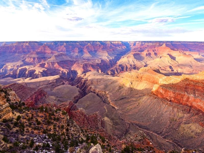 The Grand Canyon stretches away, glowing orange and purple under wispy white clouds as the sun starts to set