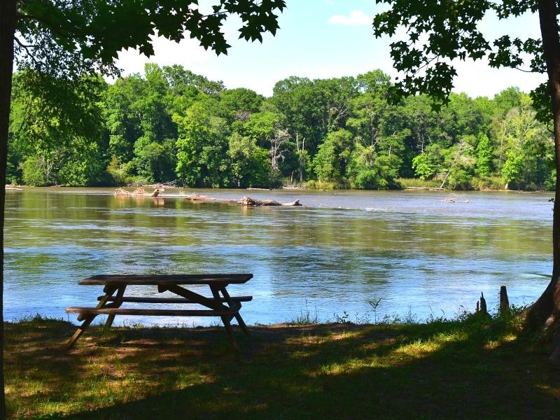 A single picnic table sits in the shade on the bank of the Catawba River