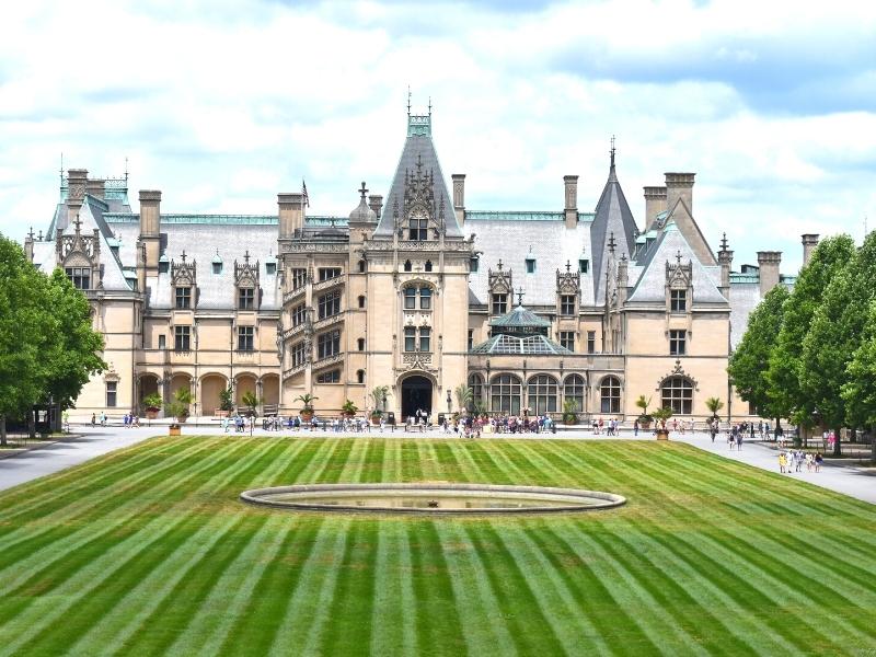 The Biltmore House on a blue and white day with its front fountain off but the green grass freshly mown
