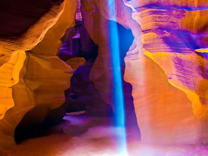 A single beam of white light illuminates a spot on the sandy floor of Upper Antelope Canyon