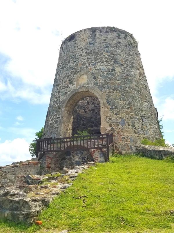 The stone ruins of Annaberg Sugar Cane Plantation's windmill sit on a green hill under a white and blue sky