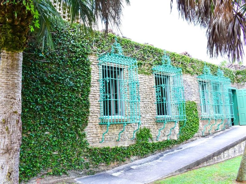 Teal wrought iron window grates pop against the tan exterior covered in green ivy at Atalaya Castle in Huntington Beach State Park