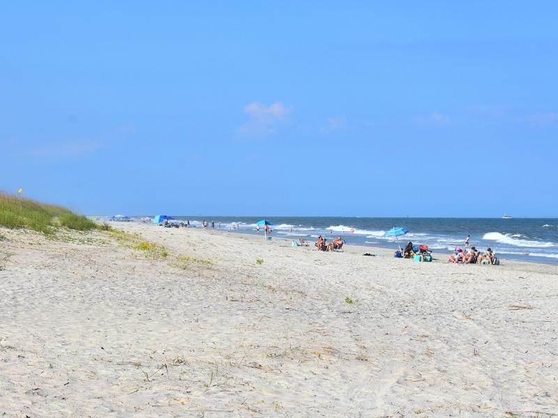 A clear blue sky over the white sand of Huntington Beach State Park with a few beachgoers in the distance