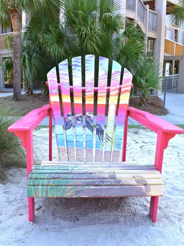 An Adirondac chair painted with a sunset scene of a pelican flying over Huntington Beach State Park