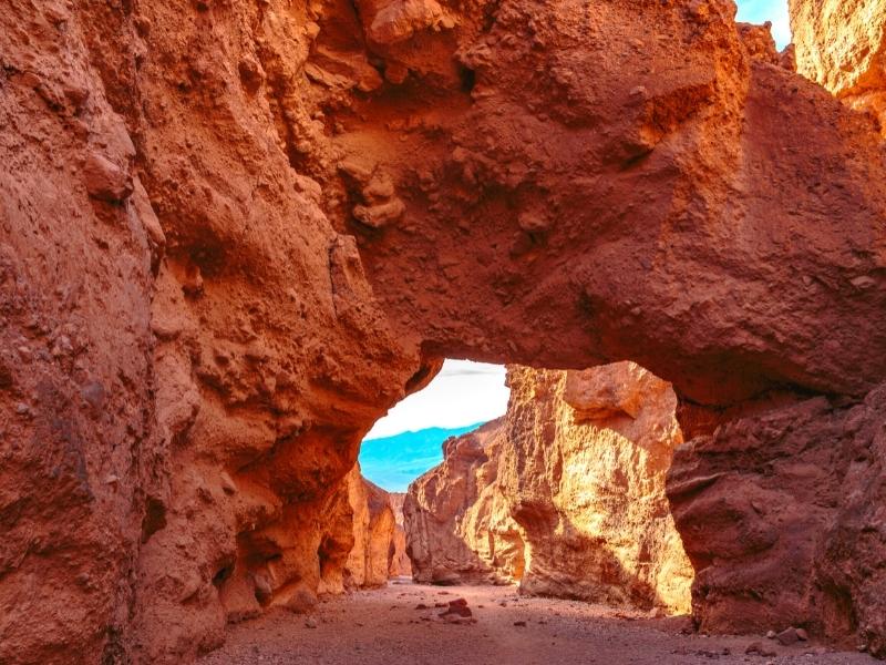 A natural rock bridge made up of orange rock and earth, with a smidge of blue sky peeking through