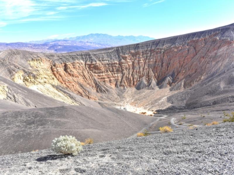 A large crater in the earth showcases the area's volcanic past with orange, yellow, and black sand at Ubehebe Crater in Death Valley