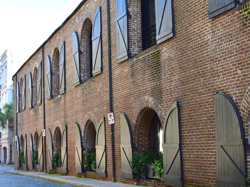 The brick exterior of a two-story building with large black shutters open remembers when this cobblestone road used to be a wharf