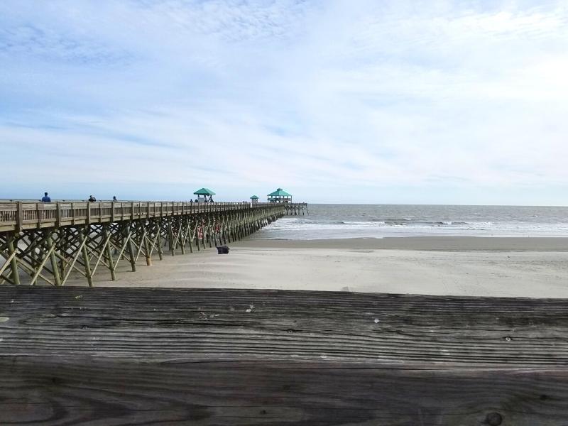 Folly Beach Pier extends into the gray Atlantic Ocean under a cloudy sky at low tide