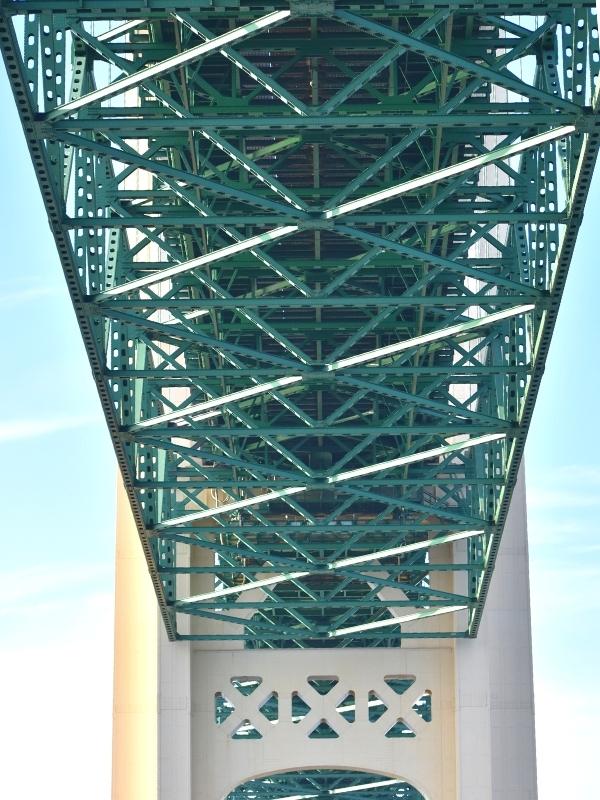 The green trusses of the underside of the Mackinac Bridge connect to the cream colored bridge pier