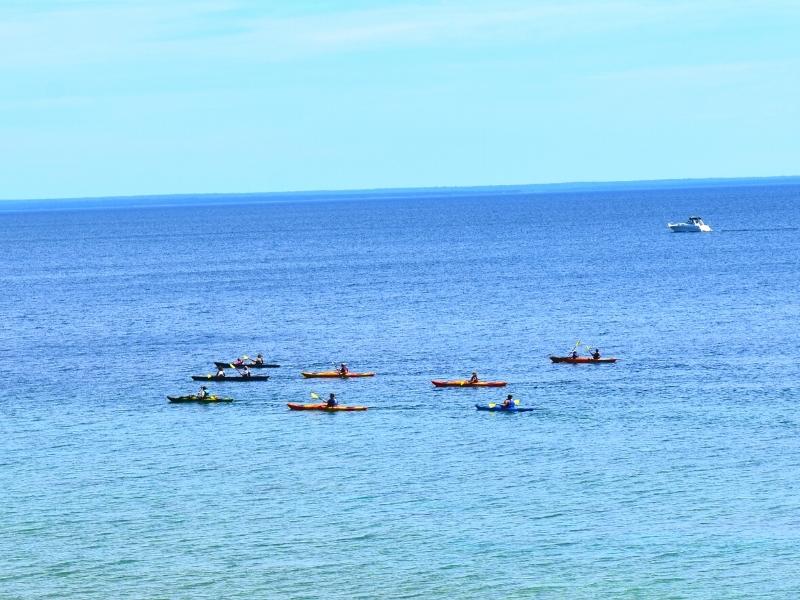 A group of kayakers paddle around Mackinac Island on the blue waters of Lake Huron with another boat in the distance