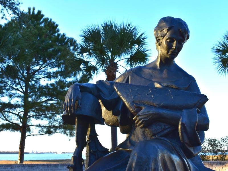 A bronze statue of a woman holding a folded American flag, her arm resting on a military helmet over a rifle at the Mount Pleasant Pier veterans memorial