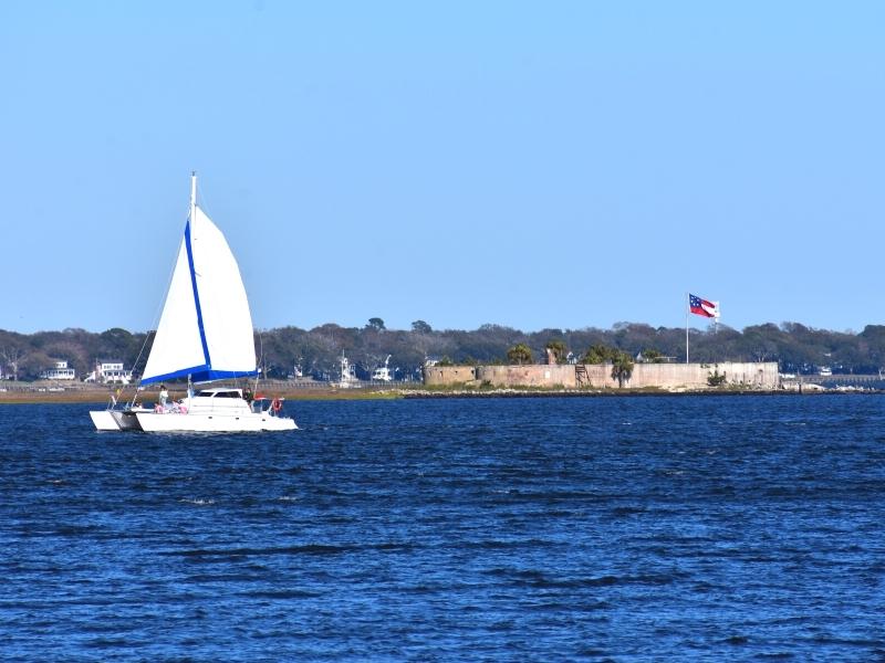 A white sailboat cruises past the ruins of Castle Pinckney in Charleston Harbor on a cloudless day