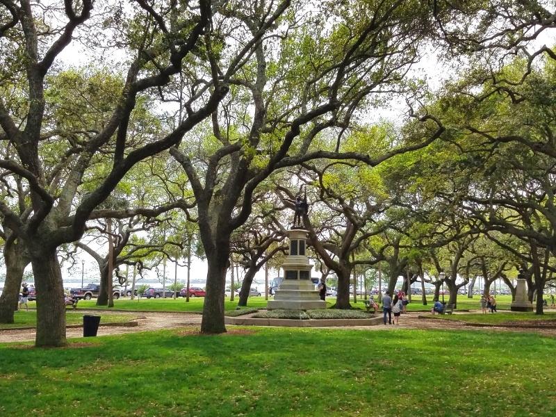 White Point Gardens features rows of giant live oak trees covered in moss over green grass and war memorials at The Battery in downtown Charleston, SC