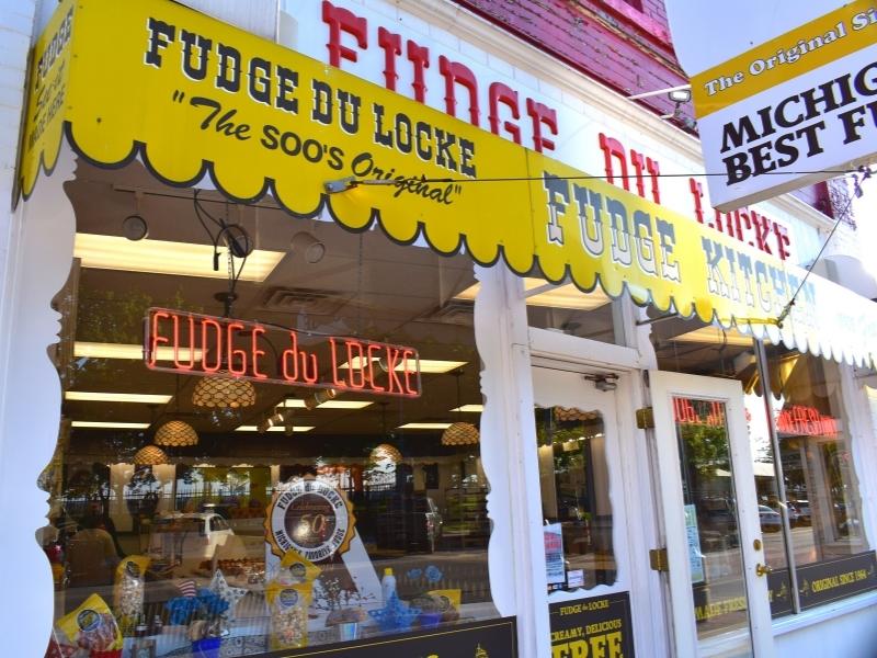 A yellow sign over Fudge du Locke fudge shop with delicious fudge treats in the window