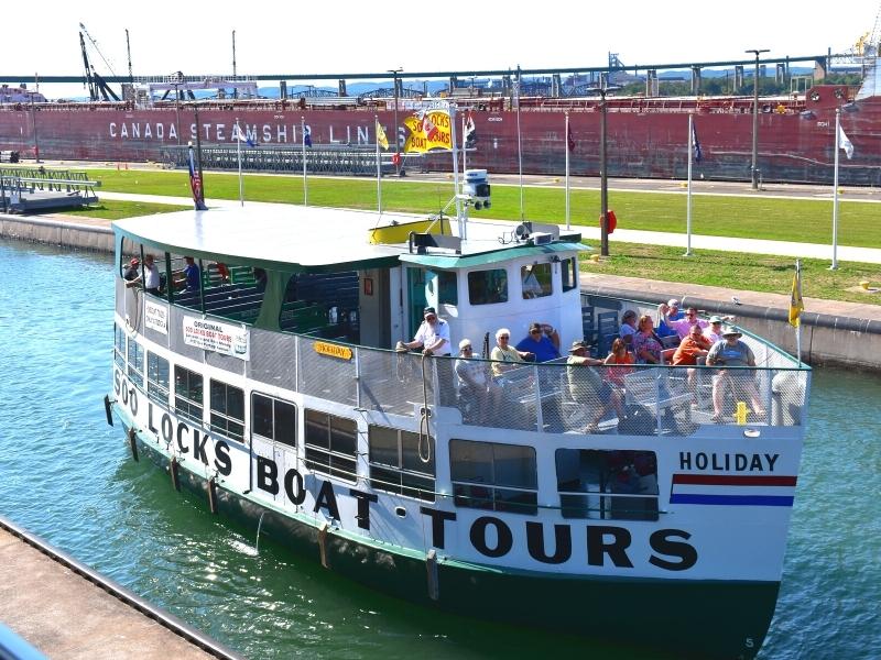 A tour boat rises in the MacArthur Lock on a sunny day as a large freighter rises in the larger lock in the background