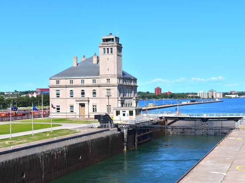 A pale stone 3 story building with a watch tower sits between the two American locks at the Soo Locks in Michigan