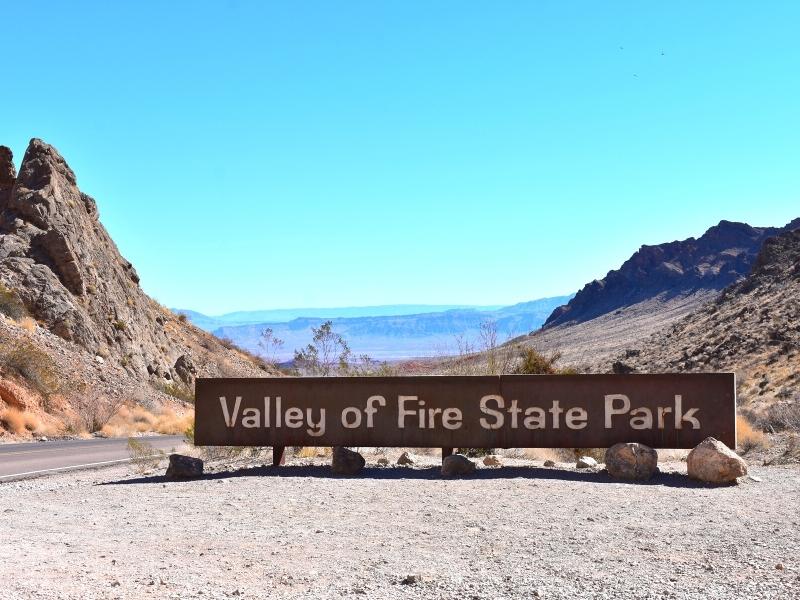 Brown Valley of Fire State Park entrance sign greets you with views of the rocky area in the distance