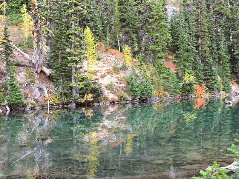 Evergreen trees with a few pops of fall color reflect in the surface of Blue Lake