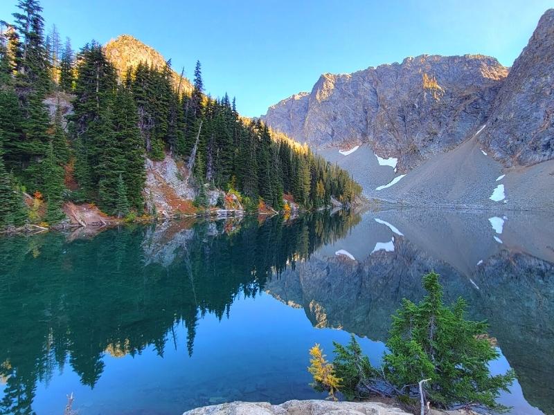 An alpine forest and mountain ridgeline grab the last golden rays of sun and reflect it all perfectly in Blue Lake in North Cascades National Park