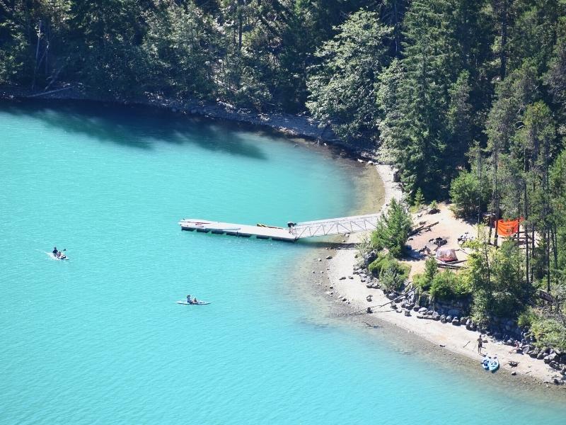 Two kayakers dot the teal blue waters of Diablo Lake near a boat ramp on Thunder Knob