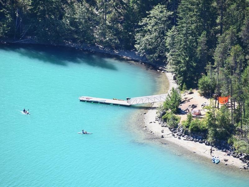 Two kayakers dot the teal blue waters of Diablo Lake near a boat ramp on Thunder Knob