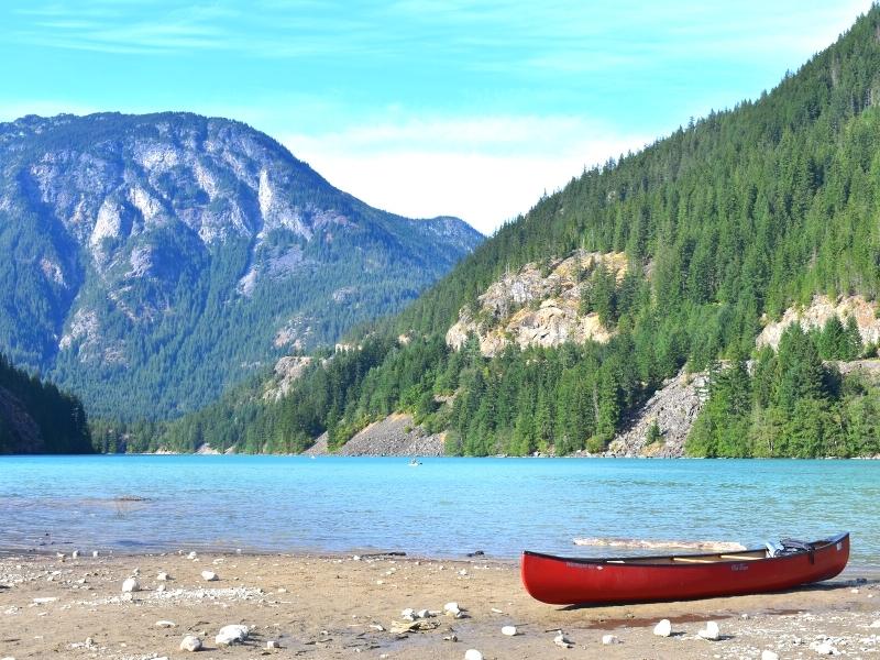 A beached red canoe sits on the shore of Diablo Lake at the Colonial Creek Campground with the green mountainsides in the background