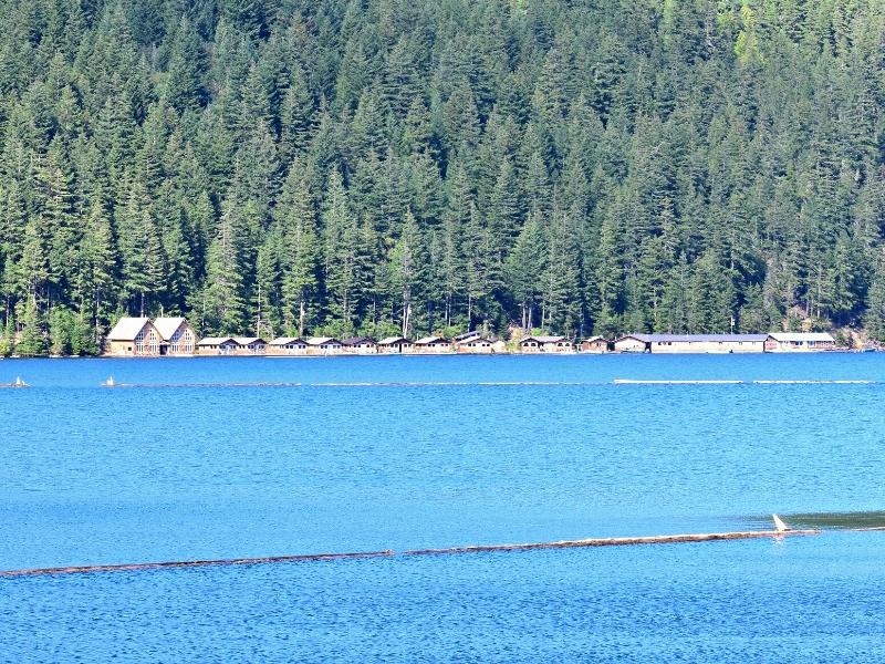Wooden buildings line the shoreline of deep blue Ross Lake with forested green mountainside behind