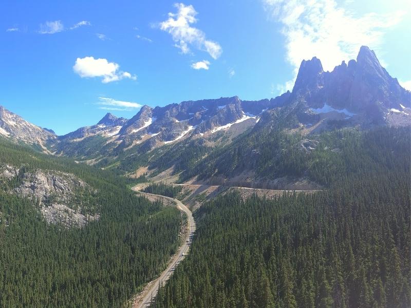 Green forested mountainside against a blue sky with North Cascades highway snaking through the Washington Pass Overlook in North Cascades National Park