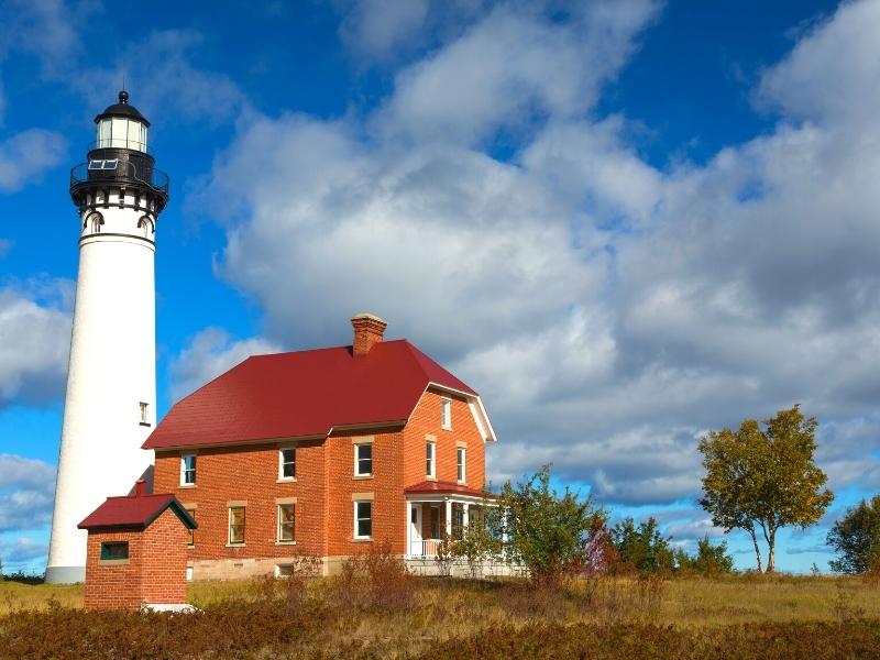 A tall white lighthouse towers above the red brick and red-roofed lightkeeper's quarters at the Au Sable Light Station in Pictured Rocks National Lakeshore