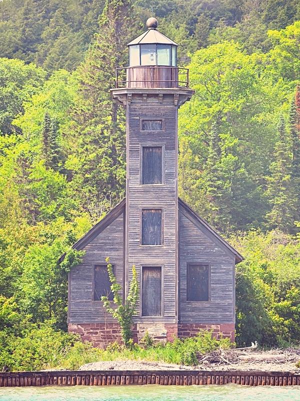 The simple wooden Grand Island lighthouse sits on the island's edge against a backdrop of bright green trees