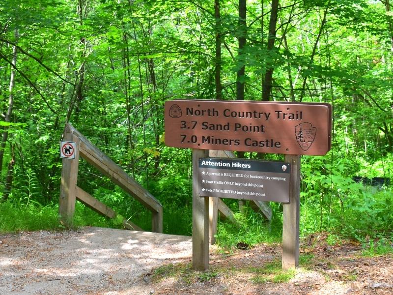 A brown trailhead sign labels the North Country Trail and distances to nearby places in Pictured Rocks