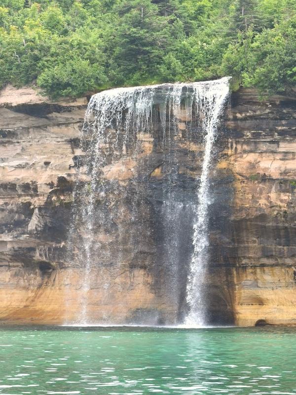 Spray Falls cascades off the tan and black cliffs of Pictured Rocks National Lakeshore and into the green waters of Lake Superior.