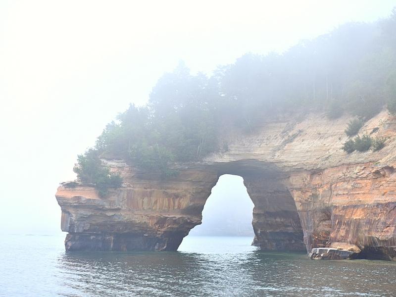 Fog partially obscures the forested archway of Grand Portal at Pictured Rocks National Lakeshore