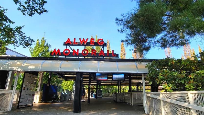 A red neon sign for the Alweg Monorail sits atop the station's roof on a clear blue day