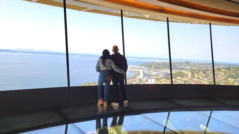 A couple hugs as they take in the views of Puget Sound from the Seattle Space Needle's enclosed glass second floor