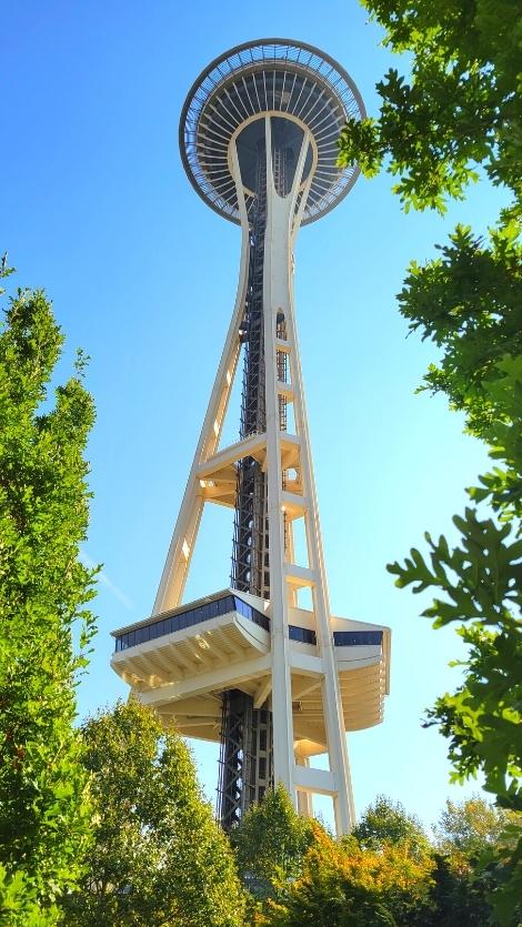 The tall yellow tower of Seattle's Space Needle as seen from the ground below against a clear blue sky